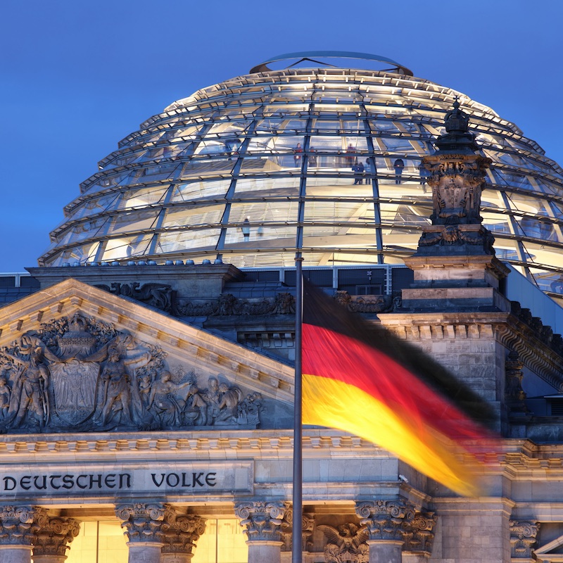 German Flag Flying Against The Reichstag In Berlin At Dusk