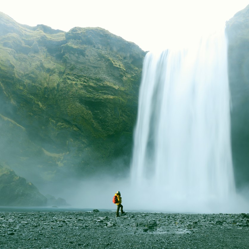 A hiker standing at a foot of a Skogafoss waterfall in Southern Iceland. Traveller looks very small in perspective with this majestic waterfall. 