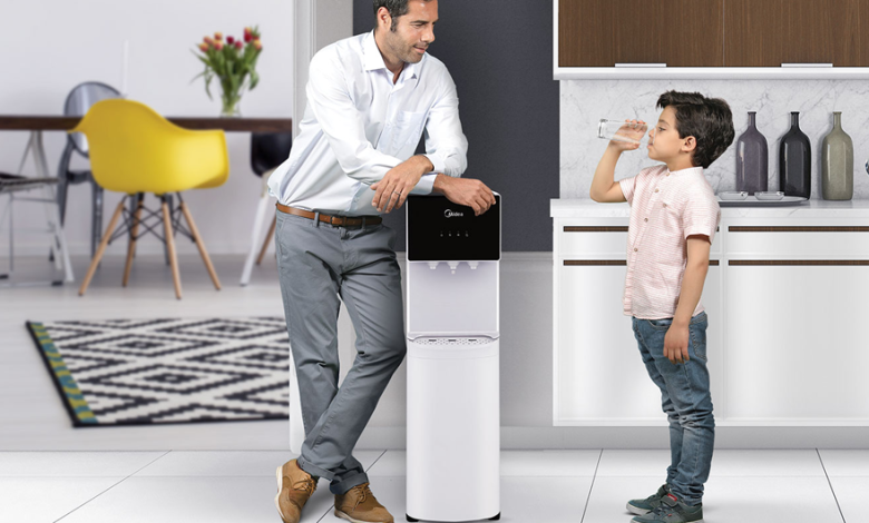 young boy drinking water from water dispenser in front of his father