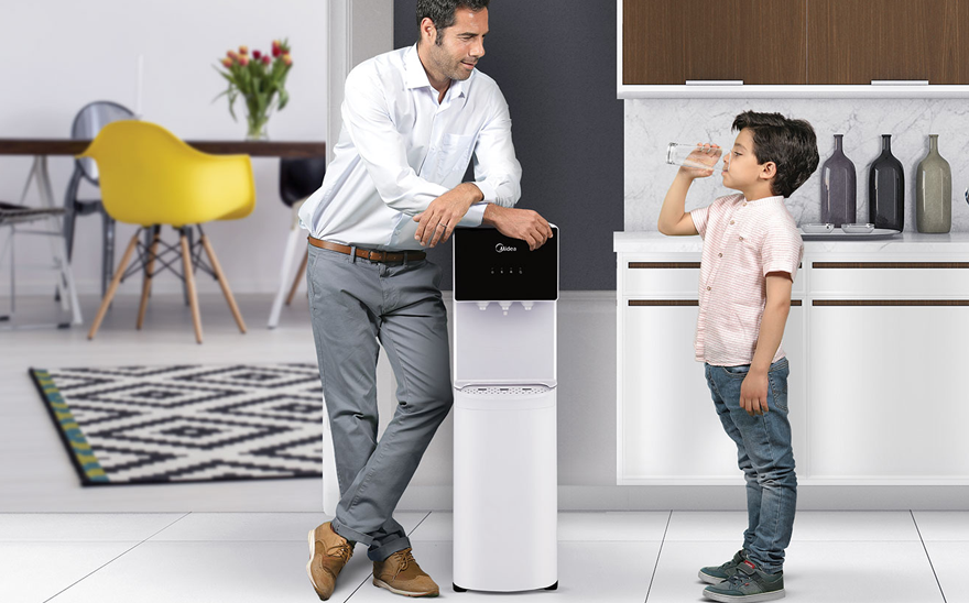 young boy drinking water from water dispenser in front of his father
